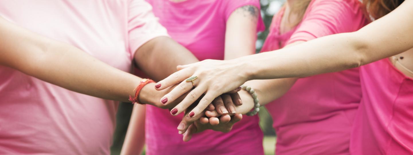 Four women wearing pink t-shirts holding hands on top of each other