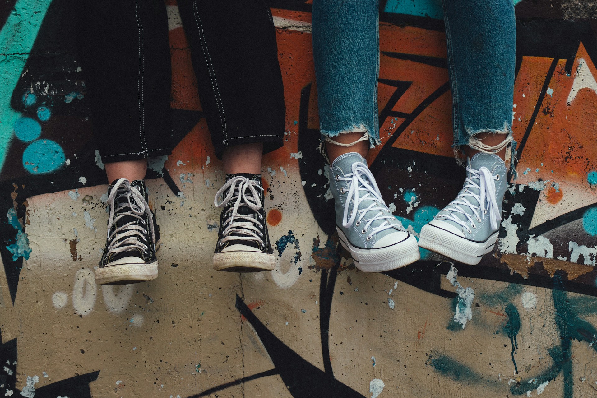 Two pairs of legs with trainers sitting on a wall with graffiti