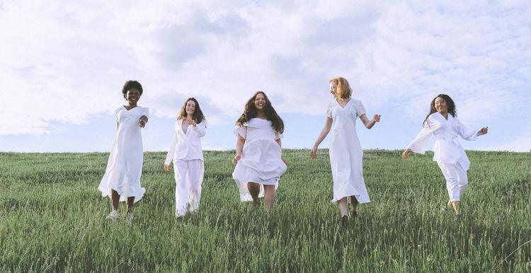 Group of women all dressed in white walking through a field 