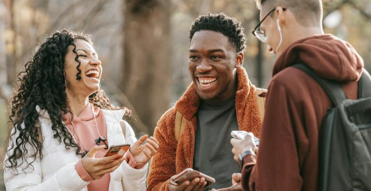 Three adults talking and laughing standing outside in a park during winter