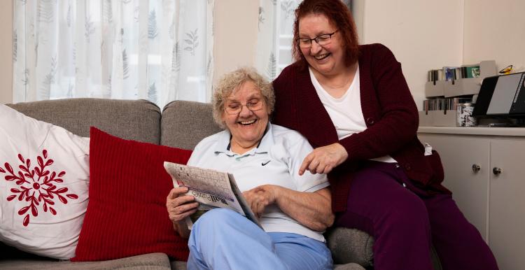 Two ladies sitting on a couch reading the newspaper