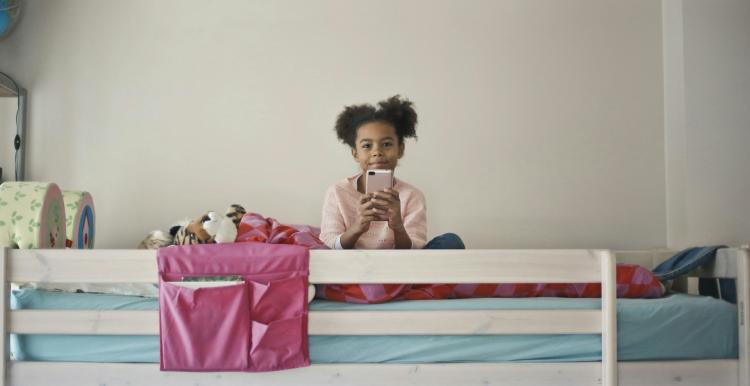 Child sitting on her bed using her mobile phone