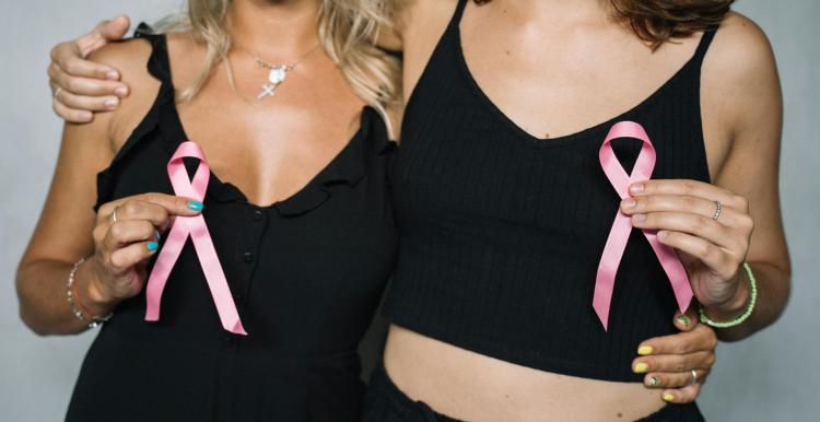 Two women dressed in black holding pink ribbons