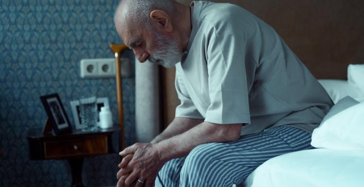 Older man worried about his mental health sitting on the end of his bed