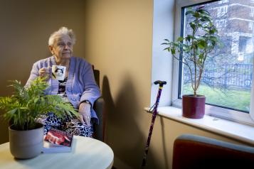 Senior lady sitting in a chair, having a hot drink and looking out of the window