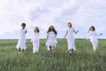 Group of women all dressed in white walking through a field 