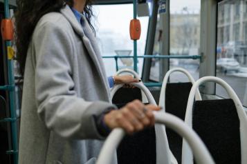 Image of a lady standing on a bus holding the bus seats