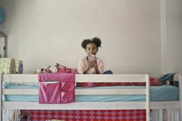 Child sitting on her bed using her mobile phone