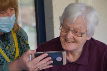 Carer and older person looking at a phone together, smiling