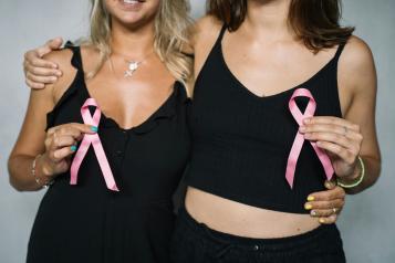 Two women dressed in black holding pink ribbons