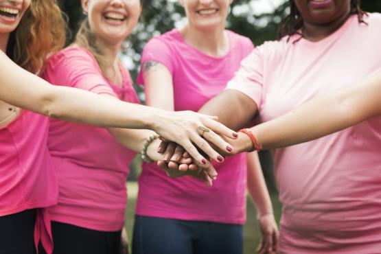 Four women wearing pink t-shirts holding hands on top of each other