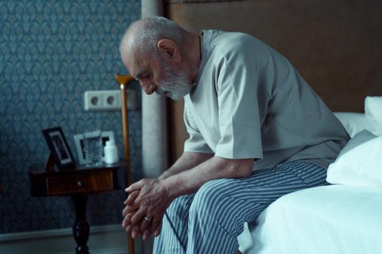 Older man worried about his mental health sitting on the end of his bed